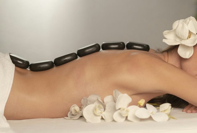 Massagem com pedras quentes nas costas, com flores brancas ao lado
