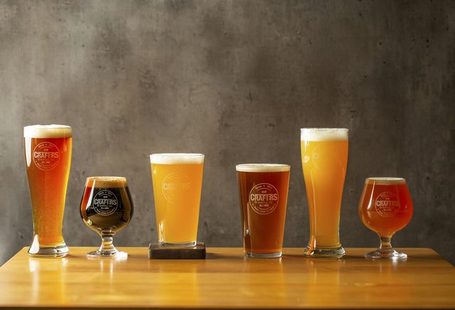 Seis copos de cerveja artesanal enfileirados num balcão de madeira