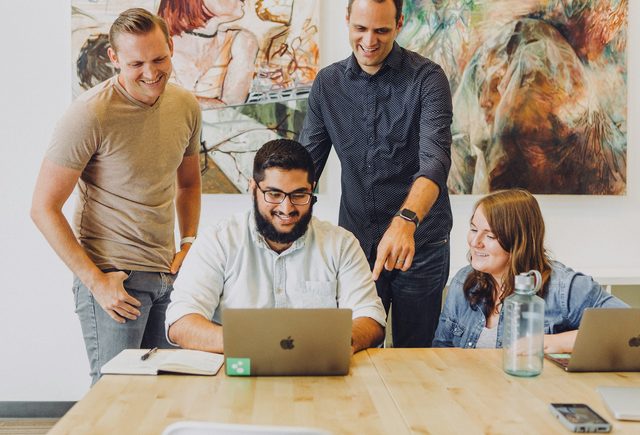 Equipe reunida em volta de um notebook numa mesa de trabalho