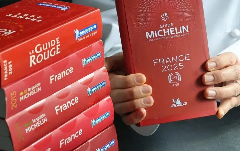 Edições do Guia Michelin empilhadas, com a de 2025 nas mãos de um chef
