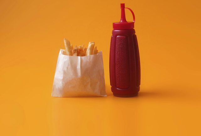 Garrafa de ketchup ao lado de um saquinho de batata frita